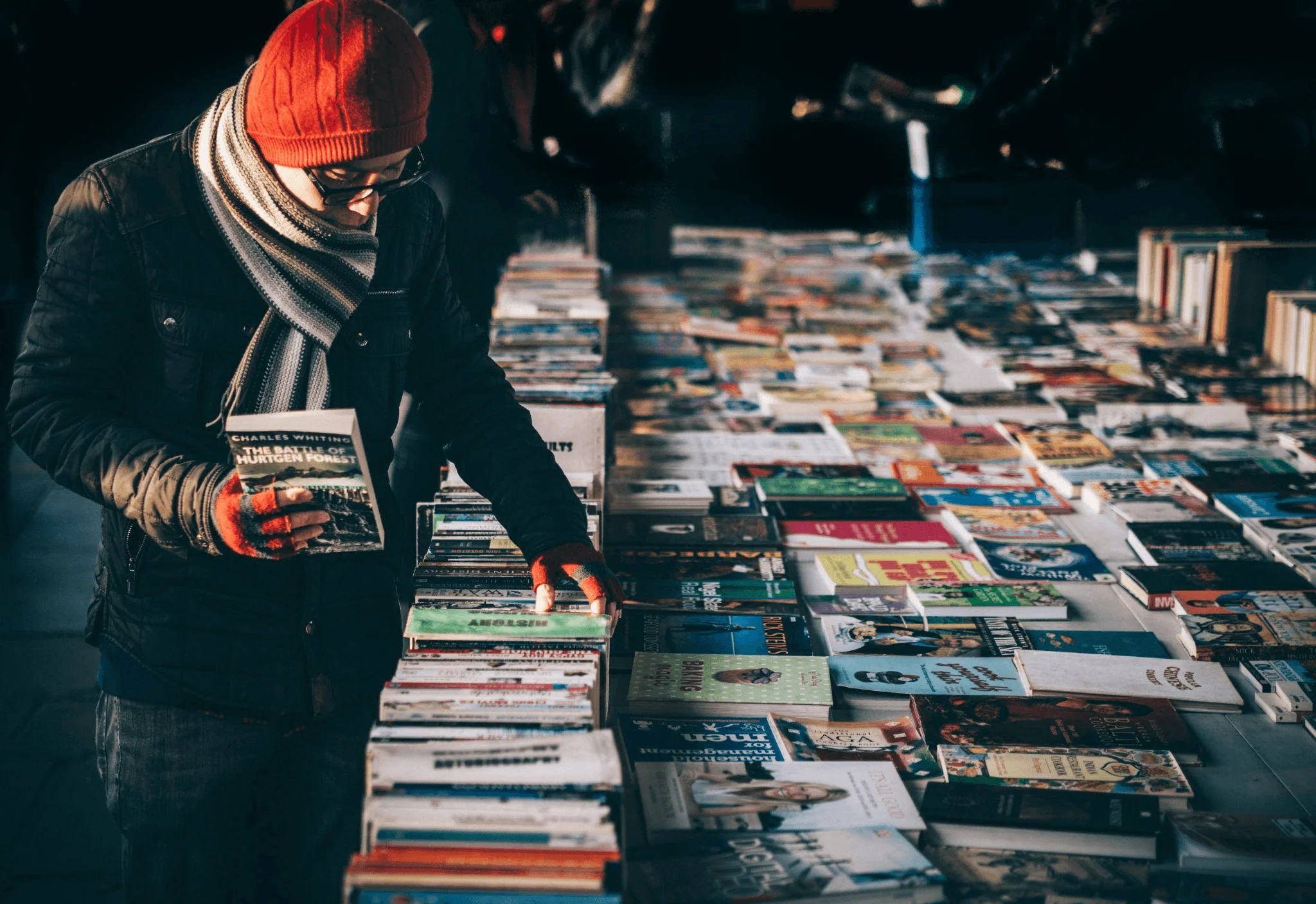 A person holding a book while browsing a colorful selection of titles, showcasing how strategic use of color in book cover design influences reader attention and perception.